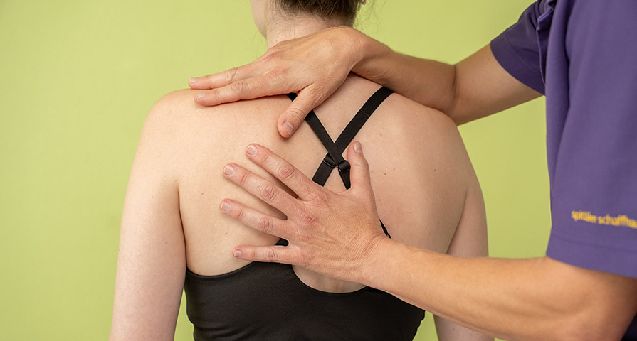 Bild einer Physiotherapeutin, die eine Patientin mittels Funktioneller Orthonomie und Integration (FOI) behandelt. Die Therapeutin hat ihre Hände auf dem Rücken und den Schultern der Patientin.