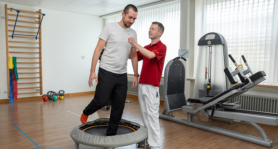 Bild eines Physiotherapeuten, der mit einem Patient, der Schwindel leidet, ein Trampolintraining macht..